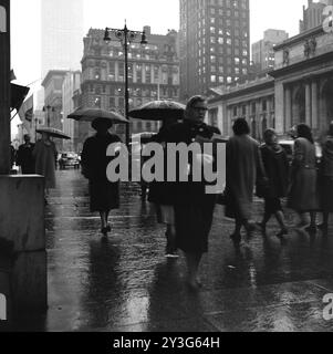 Pedestrians walk the rainy 5th Avenue in New York City near the intersection of 42nd Street and the New York Public Library. Stock Photo