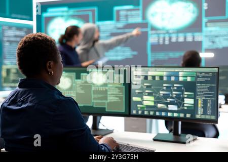 Woman governmental hacker analyzing digital threats on a computer, working in professional agency with a big screen. Specialist collecting information, fighting against cyberterrorism. Stock Photo