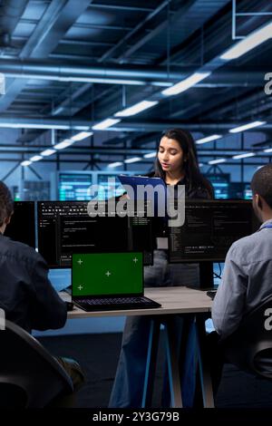 Technician inspecting server farm gear, reading paperwork from clipboard while staff members work on green screen laptop. Admins checking supercomputers with mockup notebook device Stock Photo