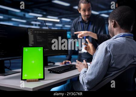 Multiethnic team using green screen tablet to oversee servers used for managing databases. Diverse staff members collaborating while working on mockup device in data center storing information Stock Photo