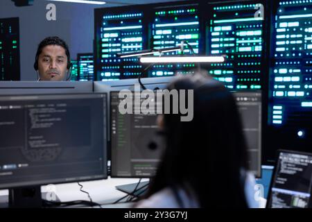 Team of professionals in data center supporting engineering team doing equipment maintenance, talking in headset microphone. Teamworking colleagues in server farm coordinating technicians using mic Stock Photo