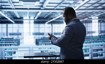System administrator in server room establishment installing newly ordered storage unit. Software developer working in data center facility housing storage rackmounts, camera B Stock Photo