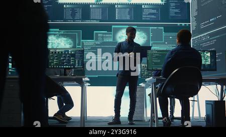 Group of governmental hackers analyzing digital threats on pc networks, using a big screen. Specialists working on collecting information, fighting against cybercrime and cyberterrorism. Camera B. Stock Photo