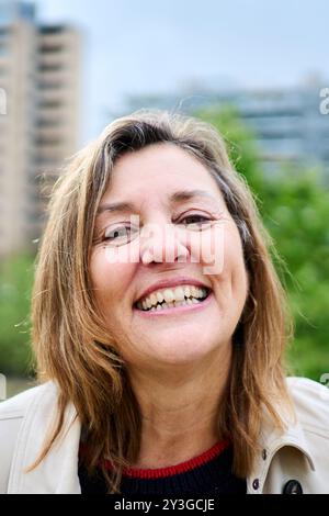 Portrait of cheerful older blonde woman posing outdoors with unfocused background urban garden. Stock Photo