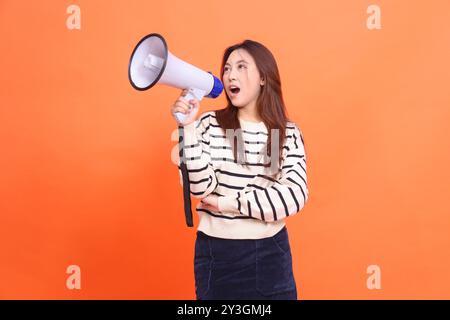 Asian woman candid screaming expression standing holding megaphone loudspeaker to announce while holding arms. for fashion, business and broadcast con Stock Photo
