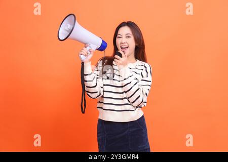 Asian woman cheerful shouting expression using mic to camera standing holding megaphone loudspeaker to make an announcement. for fashion, business and Stock Photo