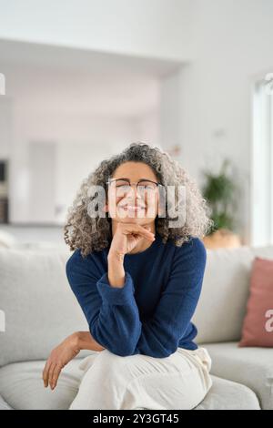 Vertical portrait of happy 50 years old woman sitting on sofa at home. Stock Photo