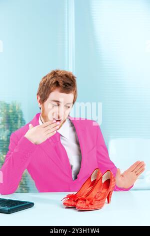 Man in a pink blazer expresses joy and surprise at receiving a quirky gift of red polka-dot shoes from colleagues Stock Photo