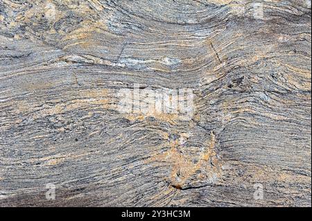 A wavy gray rock surface showcases intricate textures and subtle orange hues, reflecting natural geological formations in sunlight at an outdoor locat Stock Photo