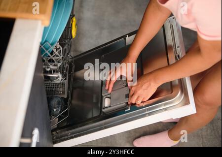 A top view of a person placing a detergent tablet in a dishwasher. The modern kitchen setting highlights home efficiency and cleanliness. Stock Photo
