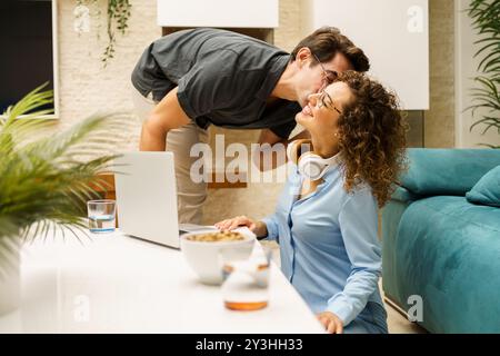 Happy couple with laptop having fun while working remotely in living room Stock Photo