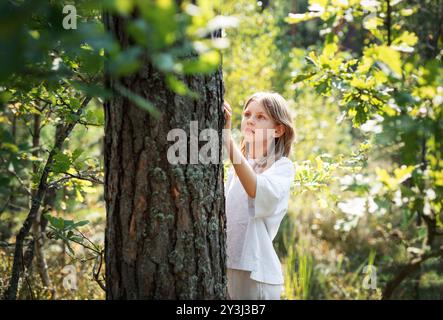 A teenage girl hugs a tree in the forest. Hugging and touching trees to reduce stress and connect with nature. Stock Photo