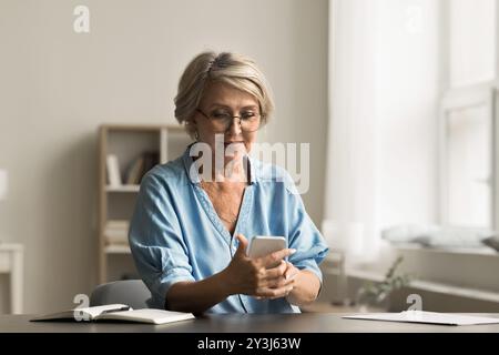 Senior woman sitting at desk using modern smartphone Stock Photo