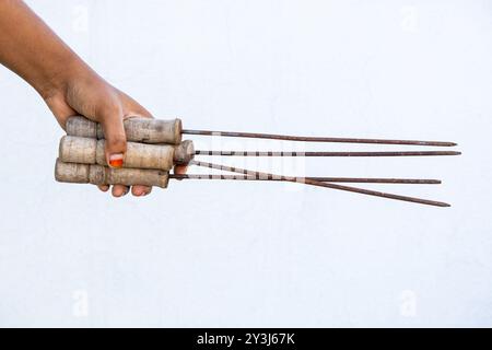 Female hand holding many rusted metal skewers with wooden handle on white background. Stock Photo