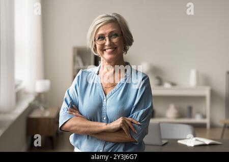 Smiling mature woman posing alone with arms-crossed indoor Stock Photo