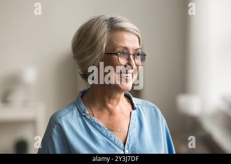 Older woman with short, grey hair standing indoor looking away Stock Photo