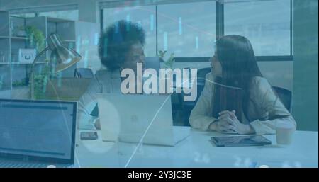 Financial data processing image over diverse businesswomen discussing in office Stock Photo