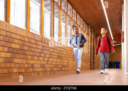 Walking in school hallway, two multiracial boy and girl with backpacks talking and smiling Stock Photo