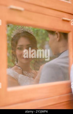 a pair of man and woman in elegant poses standing in relaxed formal poses in front of a wooden wall seen through the glass effect wearing beautiful dr Stock Photo