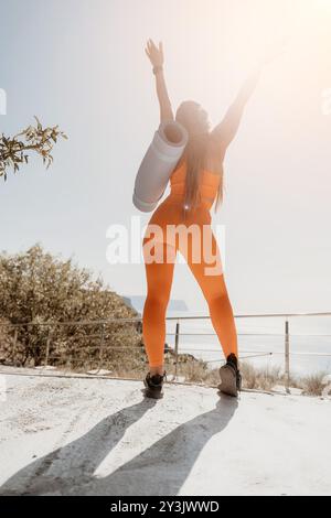 Woman in Orange Yoga Outfit Celebrating on Clifftop Stock Photo