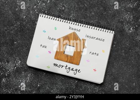 Notebook with words and wooden house figure on dark table, top view Stock Photo