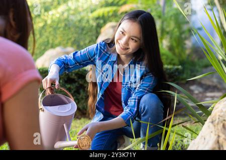 Watering plants in garden, smiling young asian woman holding watering can and kneeling Stock Photo