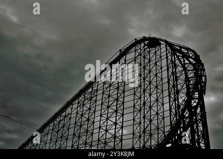 A dramatic silhouette of a roller coaster against a moody, cloudy sky. The structure is intricate, showcasing its metal framework and curves, creating Stock Photo