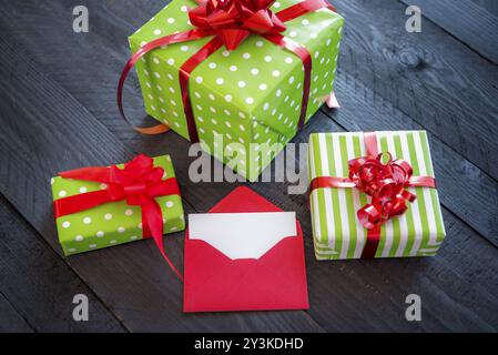 Bunch of colorful presents, wrapped in paper and tied with red ribbon and bows, with an opened envelope and blank paper, on an old wooden table Stock Photo