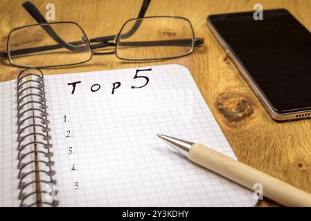 Ranking concept for a top 5 preferences list, written on a graph, spiral notebook sheet, placed on a wooden table, with eyeglasses and a phone in the Stock Photo