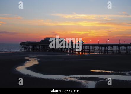 Scenic view of blackpool north pier in glowing red evening light just after sunset with illuminated pink and yellow sky and clouds with colours reflec Stock Photo