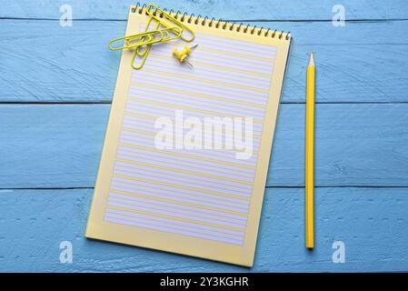 Wooden office workspace with a blank spiral notebook and crayon. Above view with yellow office supplies on a blue desk Stock Photo