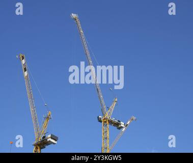 Two tall yellow construction cranes working against a blue sky Stock Photo