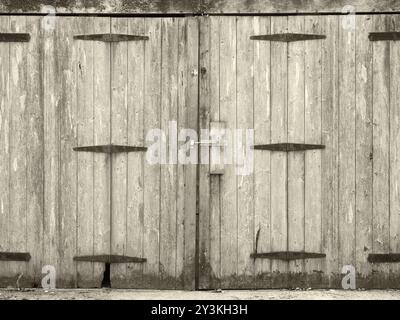Monochrome old rural grey plank wooden plank doors with a bolt fastening and rusty iron hinges Stock Photo