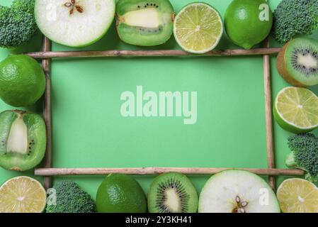 Above view of a frame made from fresh green fruits and broccoli, on a green table. Healthy eating frame. Detox context. Diet food. Vegetarian aliments Stock Photo