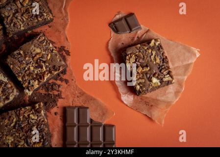 Brownie cake with walnuts sliced in pieces and chocolate chops on baking paper. Directly above view with an orange colored background Stock Photo