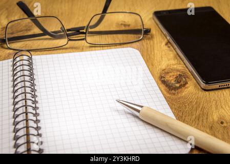 Close-up image with an opened graph, spiral notebook, eyeglasses, pen and phone on a vintage, wooden table. Perfect as a frame or background Stock Photo
