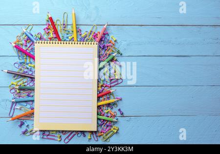 Blank page spiral notebook on a pile of office supplies, colored paper clamps, push pins and wooden crayons Stock Photo