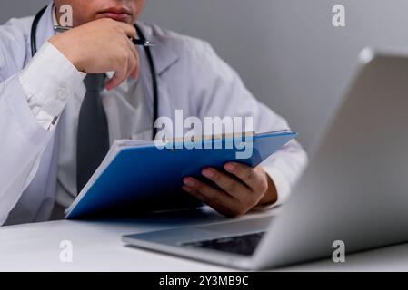 Doctor reading clipboard, thoughtful expression. Analyzing patient information, focus on diagnosis. Healthcare professional in medical office. Modern Stock Photo