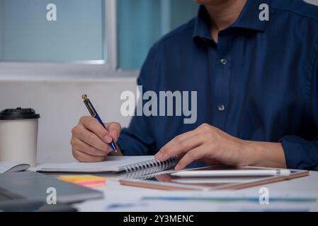 Businessman writing in notebook at office desk, planning and organizing ideas. Represents productivity, professional work environment. Ideal for corpo Stock Photo