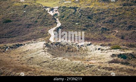 A winding dirt path through grassy hills on a sunny day in a tranquil rural landscape. Stock Photo