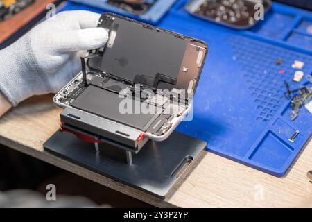 A technician performs a battery replacement on a mobile device, showcasing tools and parts in a well-organized repair workspace Stock Photo
