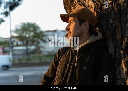 A man leaning on a tree in a park contemplates the sunset and the fall colors in the city Stock Photo