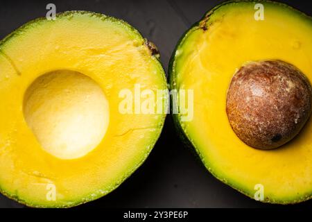 Cut avocado into two halves, one part with a pit on a black background. High quality photo Stock Photo
