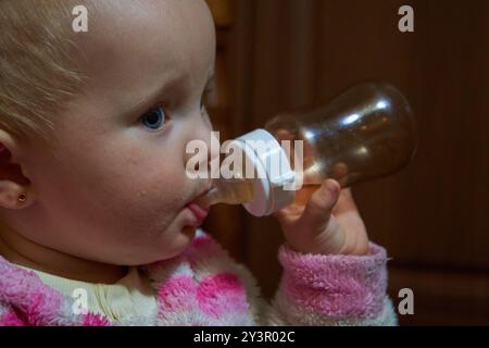 baby in a dark room drinks from a bottle of tea Stock Photo