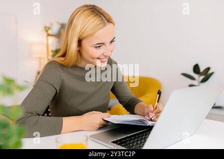 Young beautiful student woman taking notes while using laptop at home Stock Photo