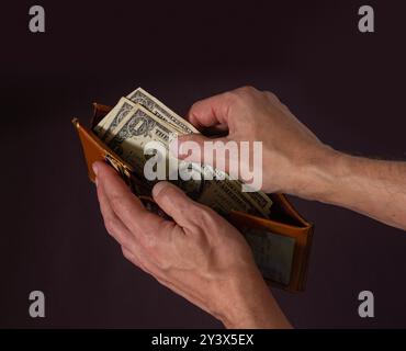 A man's hands hold open an old wallet with only three dollars left Stock Photo