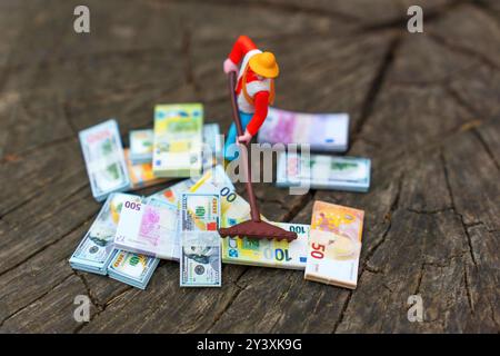 Miniature figure with rake collecting scattered money bills on wooden surface, representing financial organization or money management concept. Stock Photo