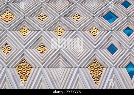 A modern architectural wall featuring a geometric pattern of alternating gold and blue shapes. The design includes diamond and triangular motifs, crea Stock Photo