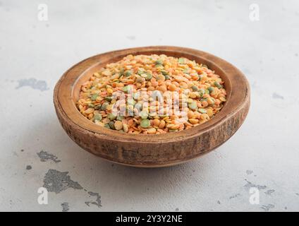 Wooden bowl of dry raw green and orange peas seeds on light table. Stock Photo