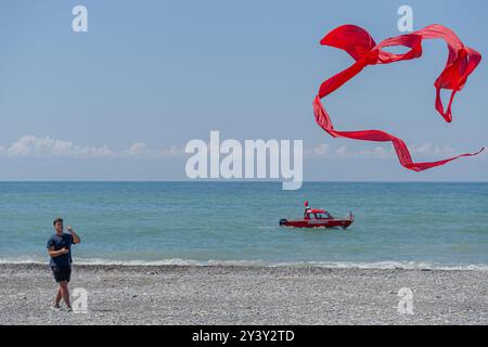 Batumi, Georgia - July 28, 2024. A man is flying a red kite on the beach. The sky is clear, the ocean is calm. Stock Photo